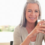 Happy senior woman drinking a glass of water in brightly lit kitchen